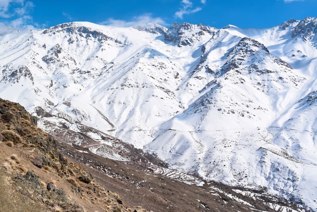 Best time to climb Toubkal — snow patches on the summit cone above a green High Atlas valley in late spring